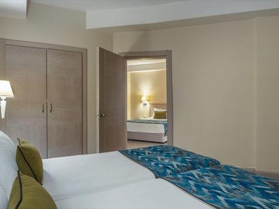 Hotelzimmer mit zwei Betten, Wand-TV und Blick auf ein Badezimmer mit Waschbecken.