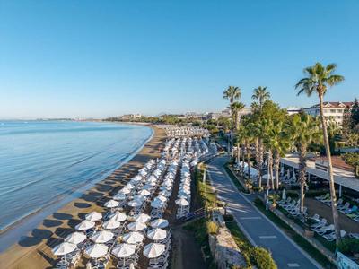 Strand mit vielen weißen Sonnenschirmen, Palmen und Spazierweg bei klarem Himmel
