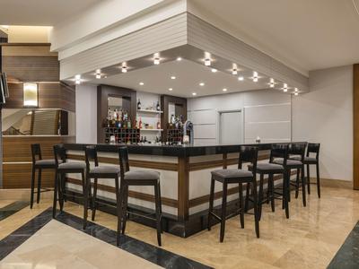 Espace bar d'hôtel moderne avec tabourets et éclairage élégant sous un plafond couvert.
