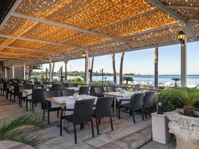 Restaurant en plein air avec tables, chaises et vue sur la mer et la plage.