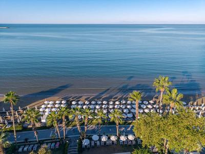 Strandansicht mit Reihen von weißen Sonnenschirmen und Palmen entlang der Küste.