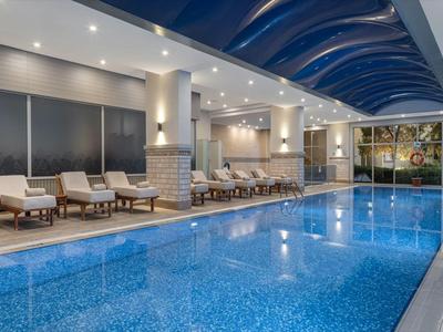 Piscine intérieure moderne dans un hôtel avec chaises longues et plafond voûté en verre.