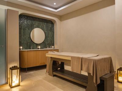 Salle de bien-être moderne avec table de massage, miroir rond et éclairage chaleureux.