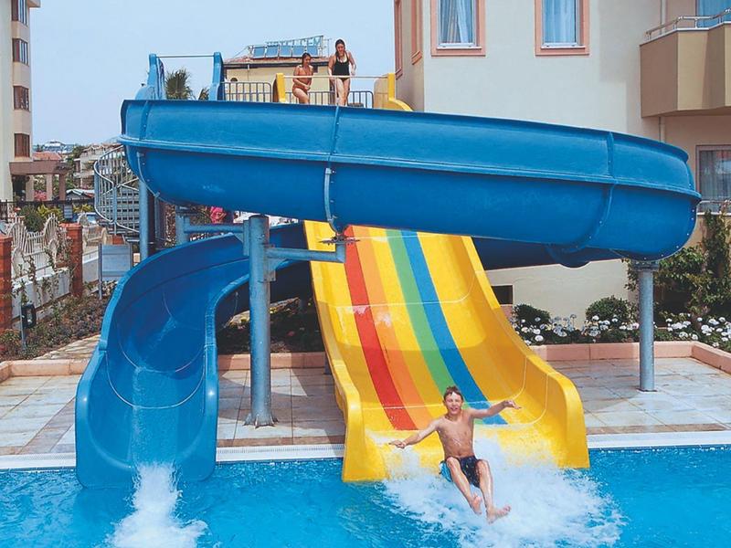 Kinder rutschen auf bunten Wasserrutschen in einen Pool vor einem Hotelgebäude.