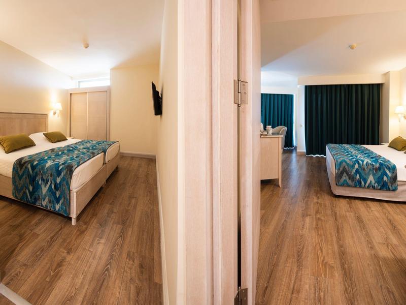 Zwei Hotelzimmer mit Doppelbetten und Holzboden, getrennt durch eine weiße Wand.