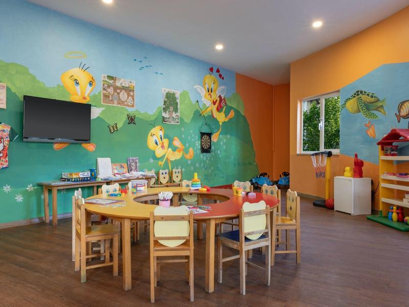 Bunter Kinderspielraum mit Rundtisch, Stühlen und Wandmalereien in einem Hotel oder Ferienort.