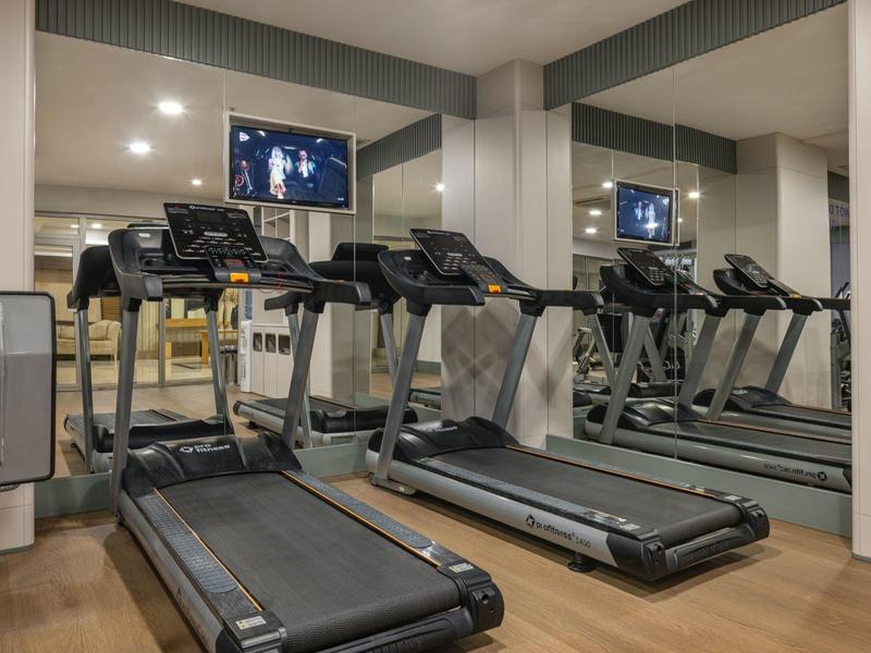 Moderne Fitnessgeräte und Fernseher in einem Hotel-Fitnessraum mit Spiegeln.