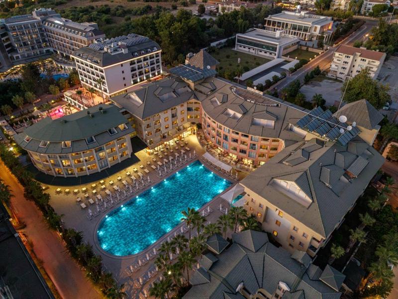 Hotelanlage mit beleuchtetem Pool und Sonnenliegen bei Nacht in einer städtischen Umgebung.