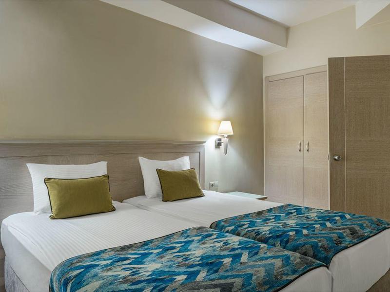 Modern eingerichtetes Hotelzimmer mit zwei Einzelbetten, Nachttischen und sanfter Beleuchtung.