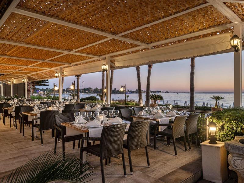 Offenes Restaurant mit gedeckten Tischen und Blick auf Meer bei Sonnenuntergang.