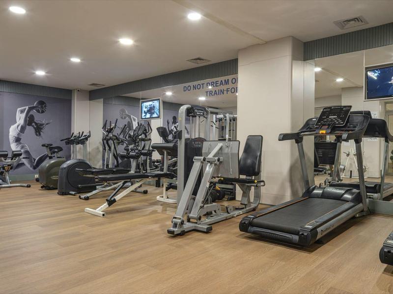 Moderner Fitnessraum mit Laufbändern, Kraftgeräten und Spiegeln in einem Hotel.