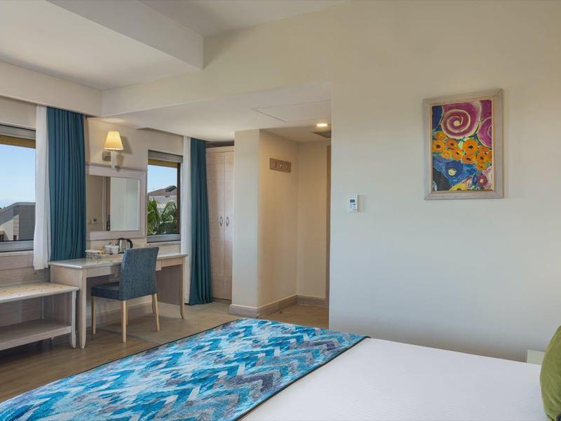 Helles Hotelzimmer mit Doppelbett, Schreibtisch, Fernseher und Fenster mit Meerblick.