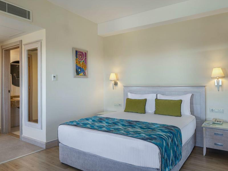 Helles Hotelzimmer mit Doppelbett, weißen Wänden und zwei Nachttischen mit Lampen.