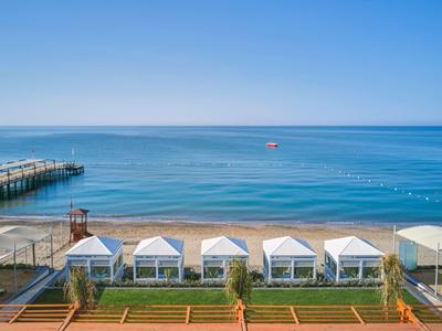 Strand mit mehreren weißen Sonnenschirmen und ruhigem, blauem Meer unter klarem Himmel.