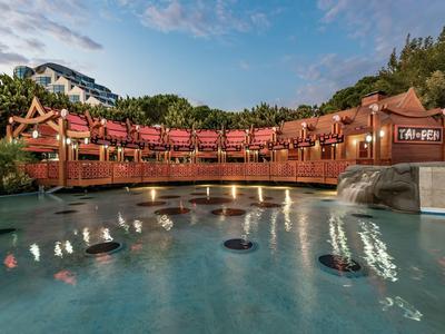 Traditionelles asiatisches Gebäude mit rotem Dach und einem Wasserbecken im Vordergrund bei Sonnenuntergang.