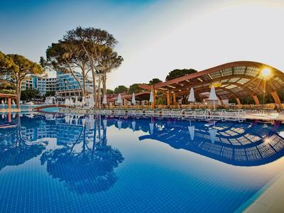 Duży basen z leżakami i nowoczesnym budynkiem w tle o zachodzie słońca.