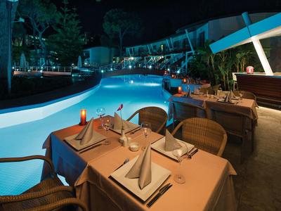 Romantisches Abendessen am beleuchteten Pool in einer Hotelanlage bei Nacht.