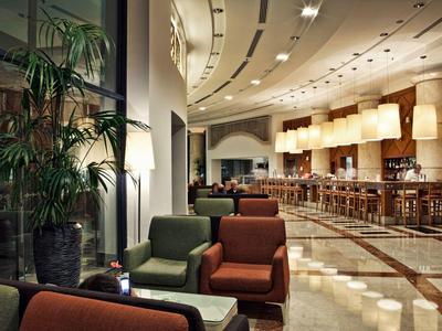 Moderne Hotel-Lounge mit farbigen Sesseln, großen Pflanzen und Bar im Hintergrund.