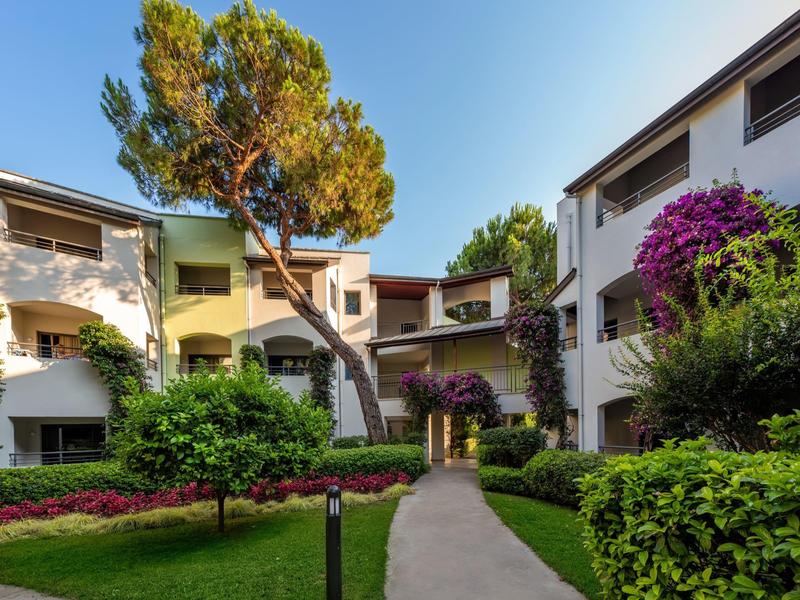 Innenhof eines Hotels mit gepflegtem Garten, Wegen und blühenden Büschen unter blauem Himmel.