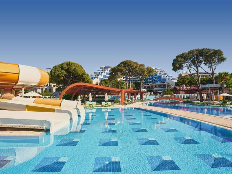 Großer Außenpool mit Wasserrutschen und klar blauem Himmel in einem Ferienresort.