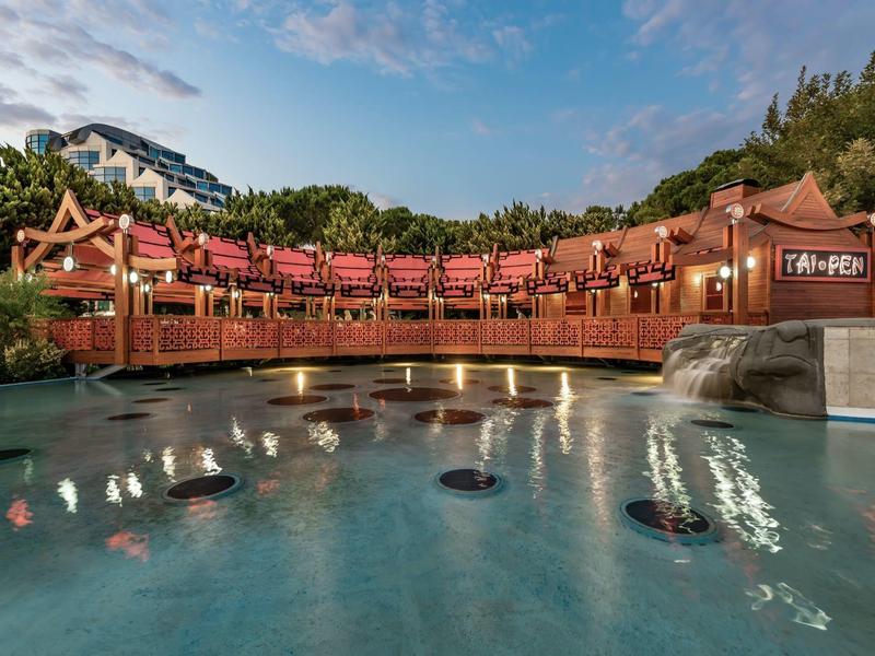 Traditionelles asiatisches Gebäude mit rotem Dach und einem Wasserbecken im Vordergrund bei Sonnenuntergang.