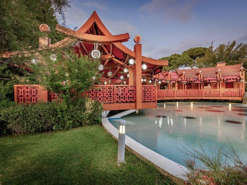 Rotes Holzrestaurant mit Terrasse neben einem Pool und umgeben von Grün.