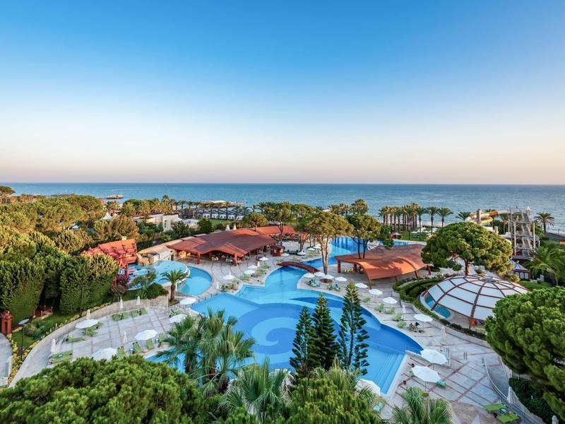 Weitläufiges Hotelresort mit mehreren Pools und Blick auf das ruhige blaue Meer bei klarem Himmel.