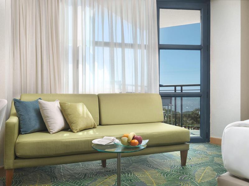 Zimmer mit grünem Sofa, bunten Kissen und Meerblick durch Fenster und Balkon