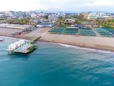 Spiaggia con molo e sdraio, hotel sullo sfondo e cielo nuvoloso.