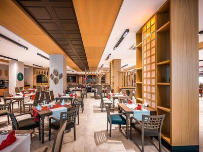 Ristorante moderno con soffitto in legno, tavoli e sedie, elementi decorativi e illuminazione brillante.