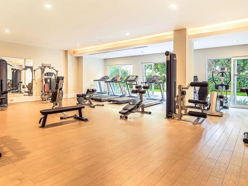 Ampia palestra con pavimento in legno e attrezzature moderne, due finestre con vista sul verde.