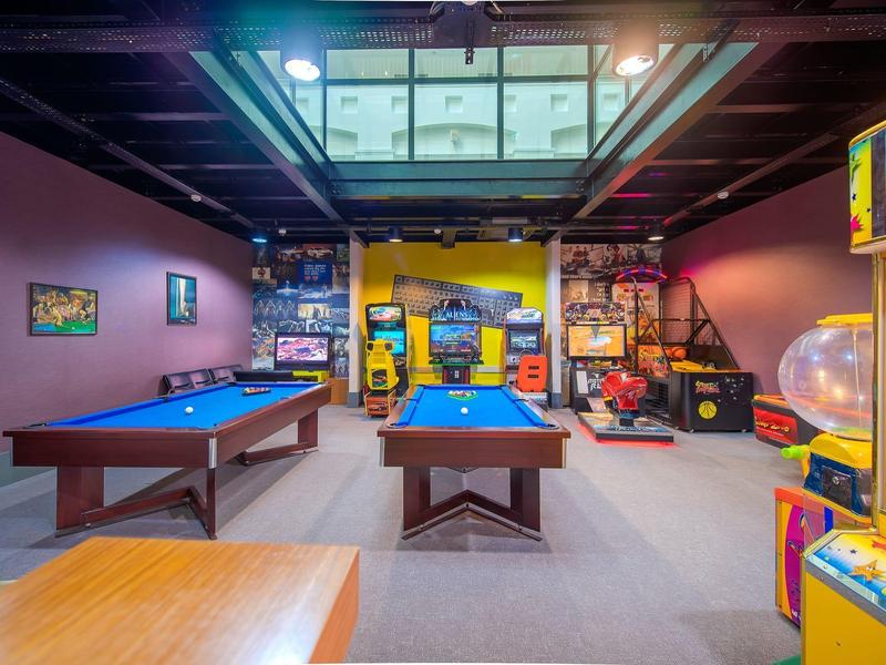 Sala giochi con tavoli da biliardo e macchine arcade in uno spazio moderno e elegante.