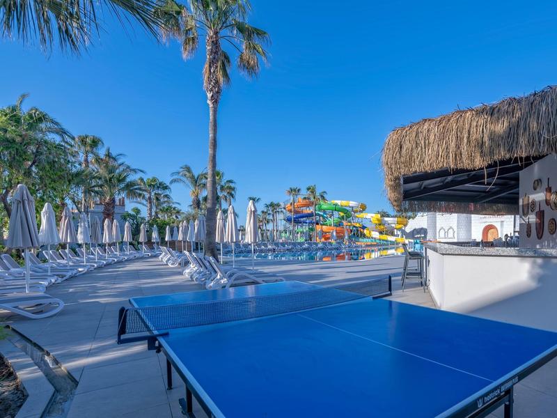 Area esterna dell'hotel con tavolo da ping pong, piscina, sdraio e scivoli d'acqua.