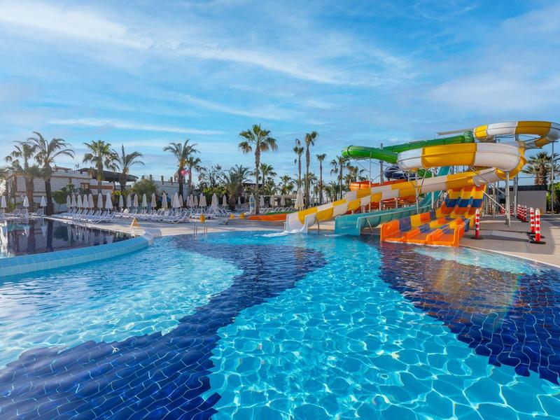 Una grande piscina all'aperto con scivoli e palme in una giornata di sole.