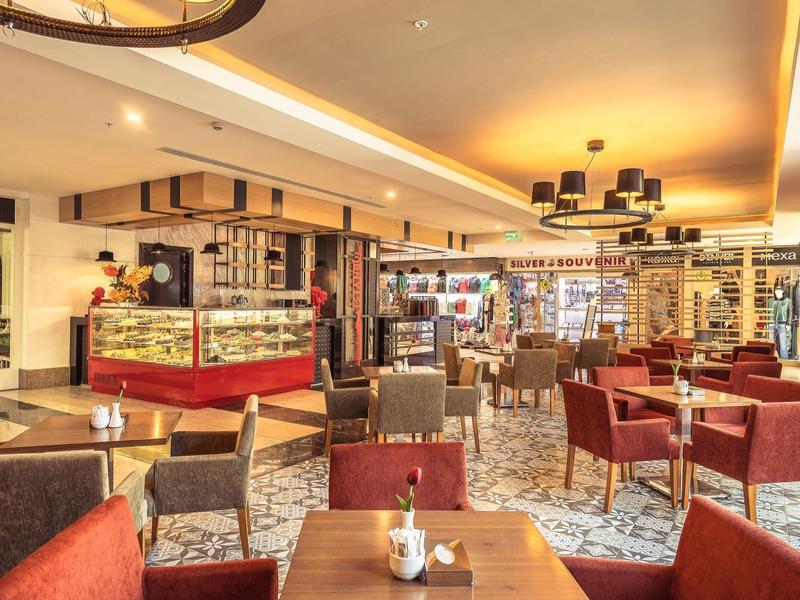 Caffè accogliente con poltrone marroni, tavoli in legno e banco rosso.