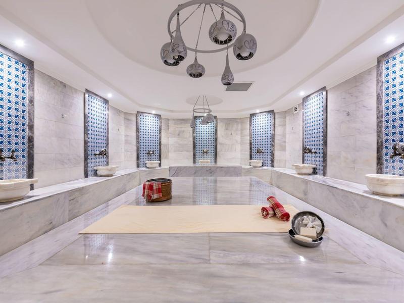 Ampio hammam turco con pareti e pavimento in marmo, più lavandini e illuminazione moderna.
