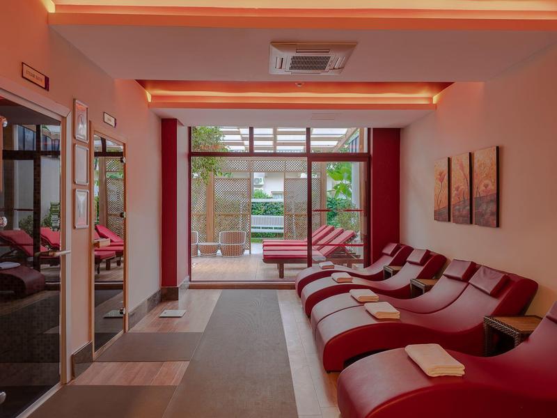 Area benessere moderna con lettini rossi e vista su una terrazza con piante verdi.