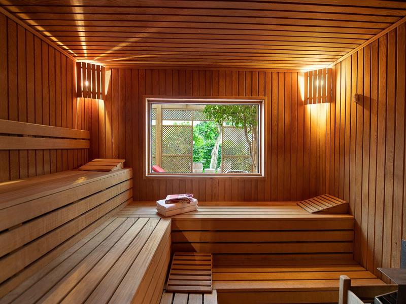 Interno di una sauna finlandese con panche in legno e una finestra che guarda il verde.