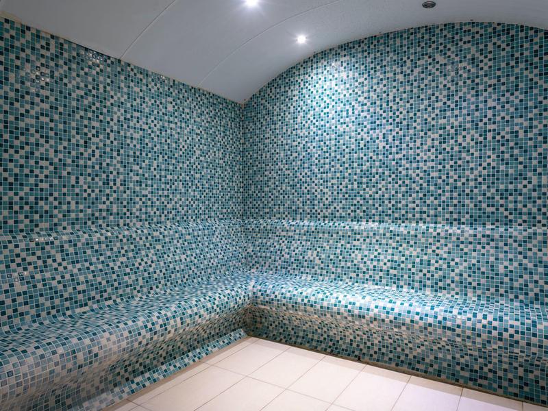 Sauna interna con pareti e area salotto rivestite di piastrelle a mosaico blu