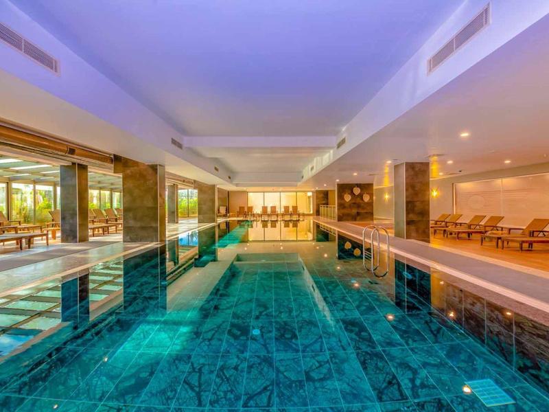 Piscina interna con acqua turchese, pannelli di legno e sedie a sdraio nell'area dell'hotel.