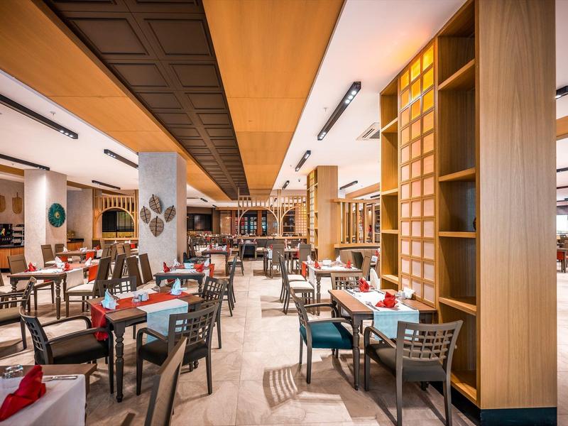 Ristorante moderno con soffitto in legno, tavoli e sedie, elementi decorativi e illuminazione brillante.