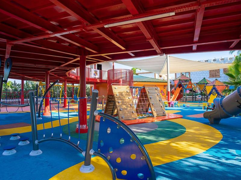 Area giochi colorata per bambini con strutture per arrampicarsi, scivoli e area coperta.