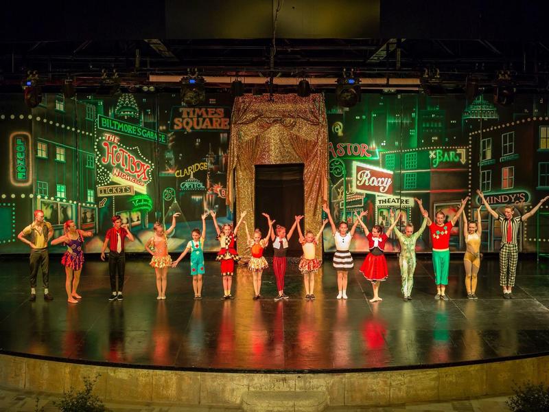 Escenario teatral con artistas en diversos disfraces haciendo reverencia final.