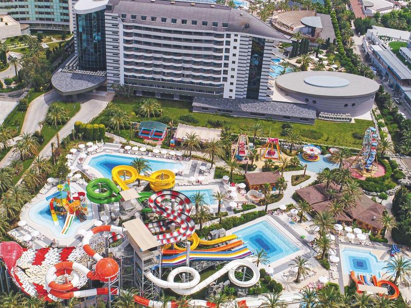 Gran complejo hotelero con parque acuático colorido, piscinas y toboganes, rodeado de palmeras.