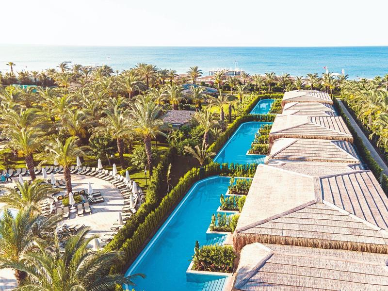 Complejo hotelero de lujo con piscina, rodeado de palmeras y vista al mar.