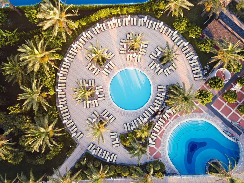 Vista aérea de una piscina redonda con tumbonas y palmeras en un complejo hotelero