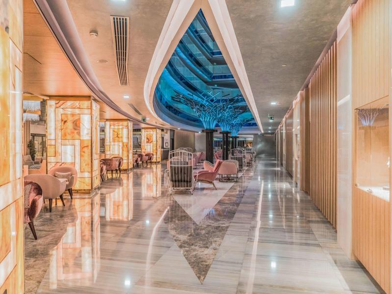 Lobby de hotel lujosa con suelo de mármol brillante, asientos elegantes y luz decorativa en el techo.