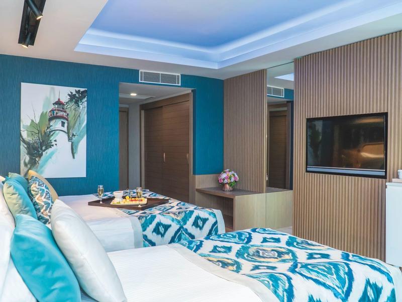 Habitación de hotel moderna con dos camas, acentos azules y iluminación indirecta en el techo.