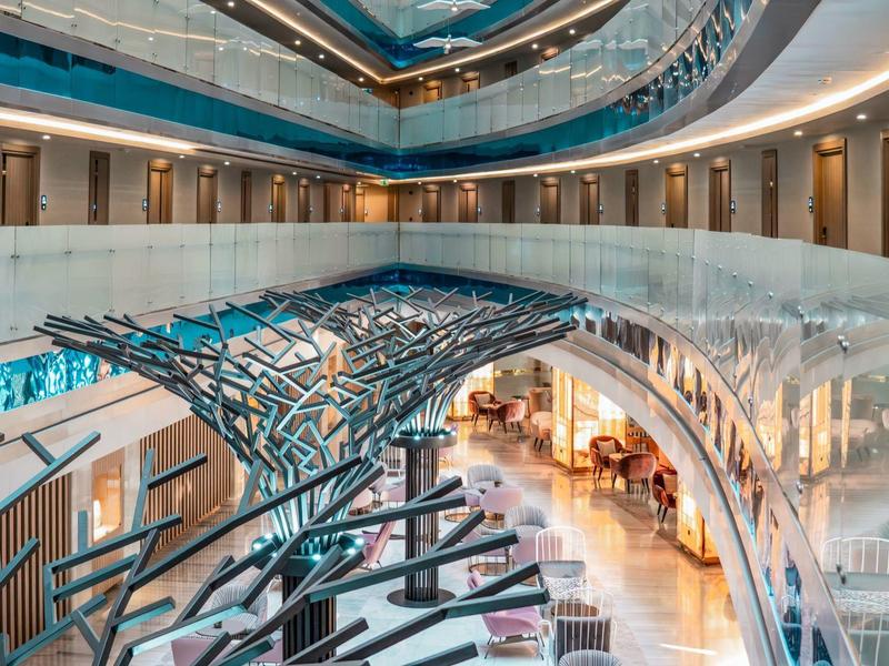 Interior moderno de hotel con puente de vidrio, líneas curvas y iluminación indirecta.