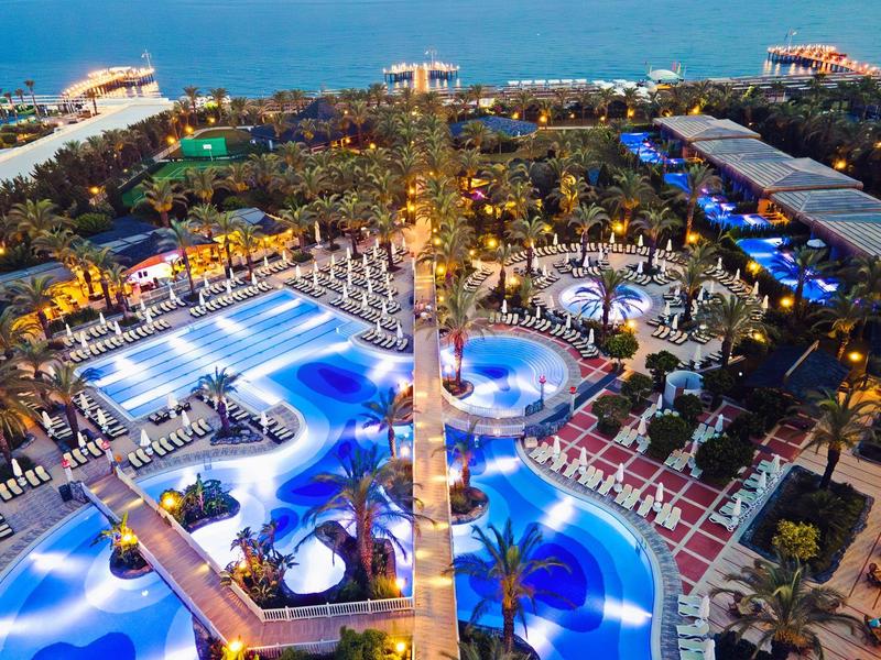 Vista aérea nocturna de una piscina de hotel de lujo iluminada con sillas y vista al mar.